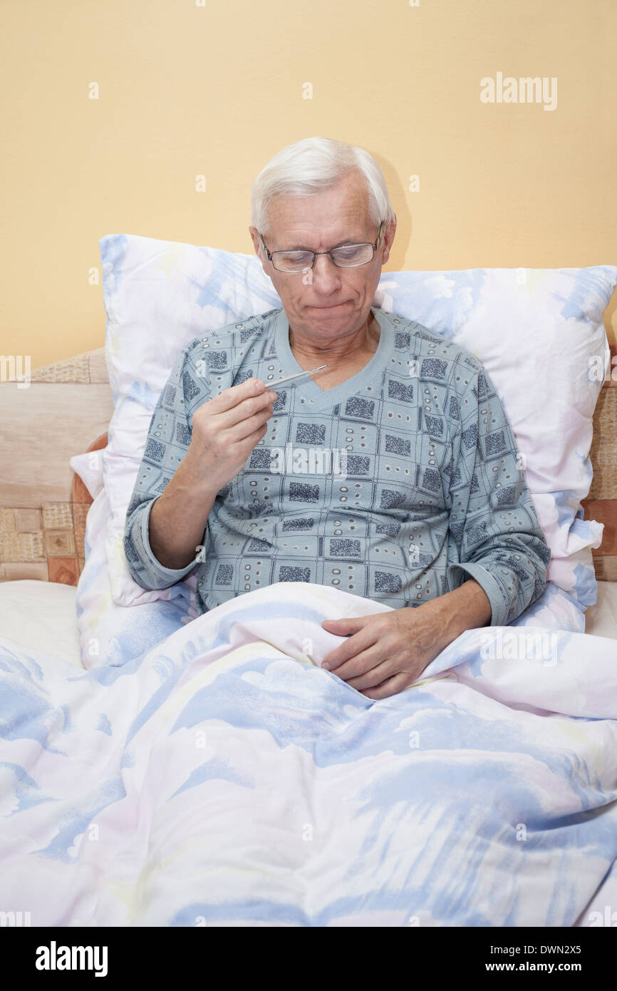 Ill senior man checking temperature with thermometer in bed. Stock Photo