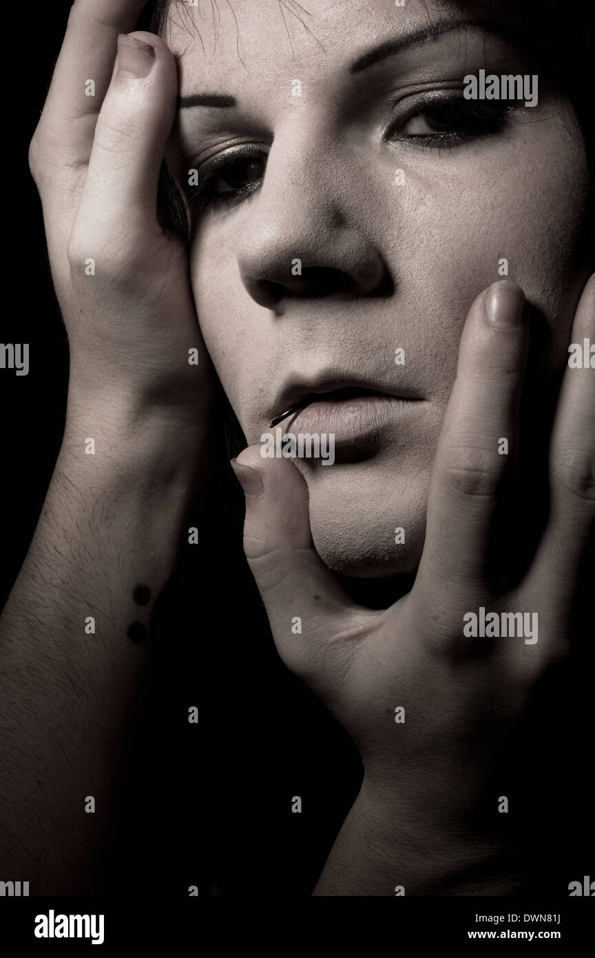 A moody face shot of a man with hands touching his face, a mysterious
