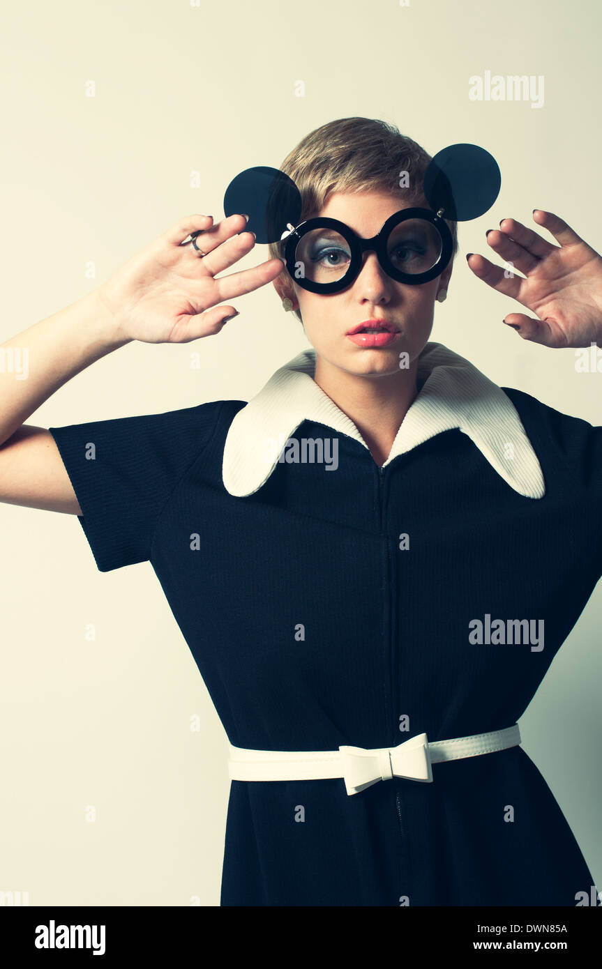 A retro woman posing in a mod 60s dress, posing with flip up round sunglasses, hands up, a retro 60s vintage fashion concept Stock Photo