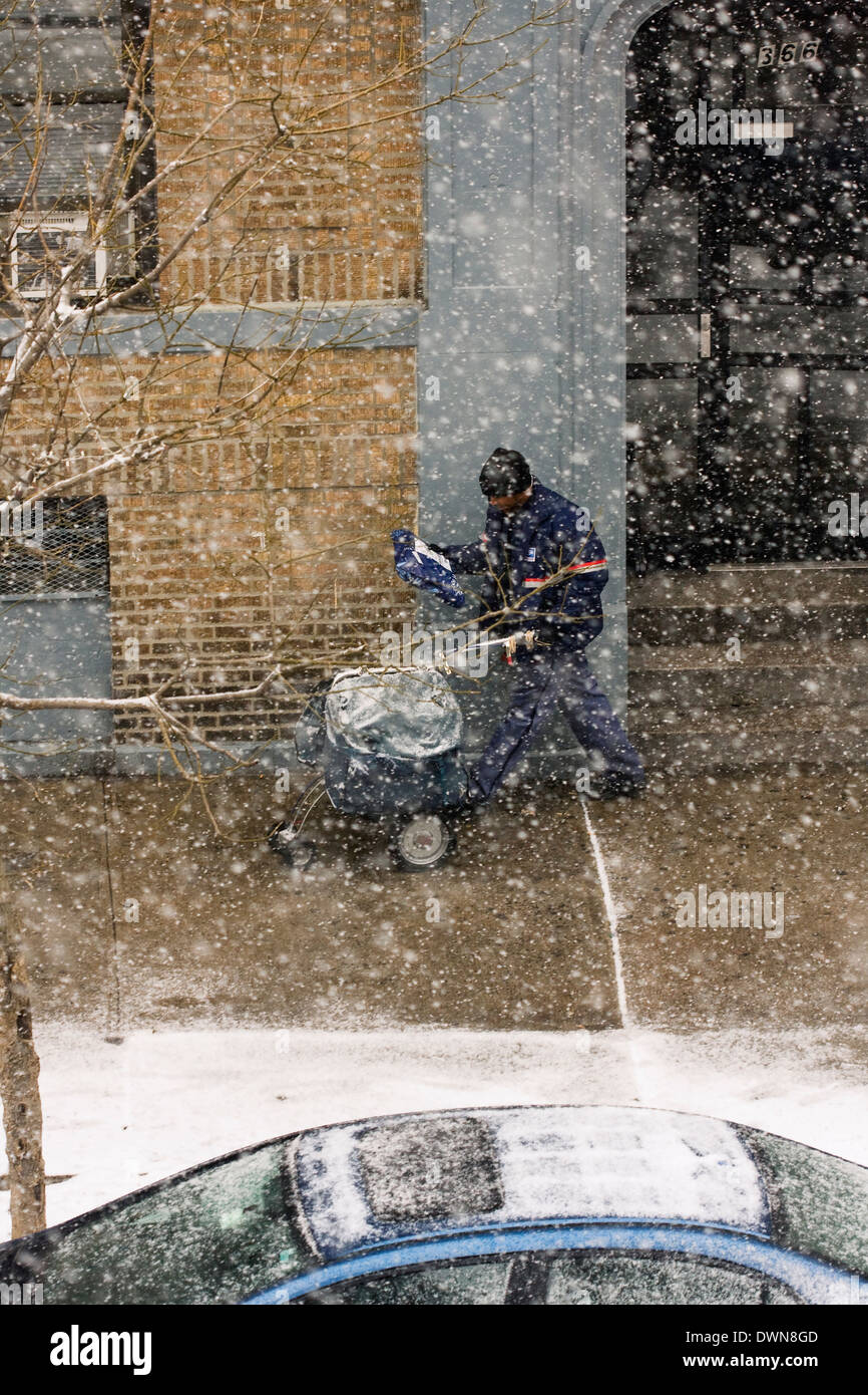 A New York City Mailman walking on the sidewalk pushing a cart whilst delivering mail and packages during a snowstorm Stock Photo