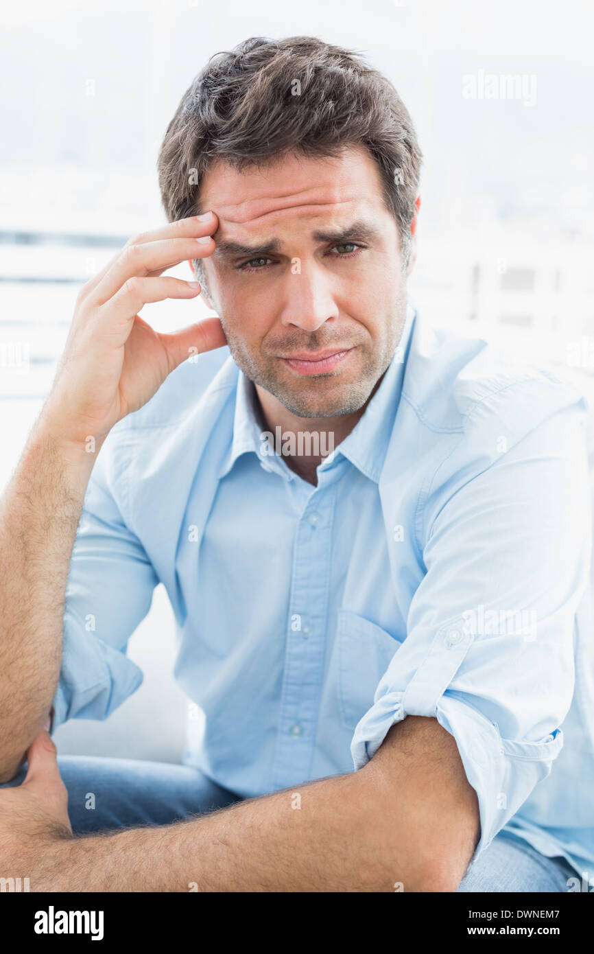 Wincing man with headache sitting on the couch looking at camera Stock Photo