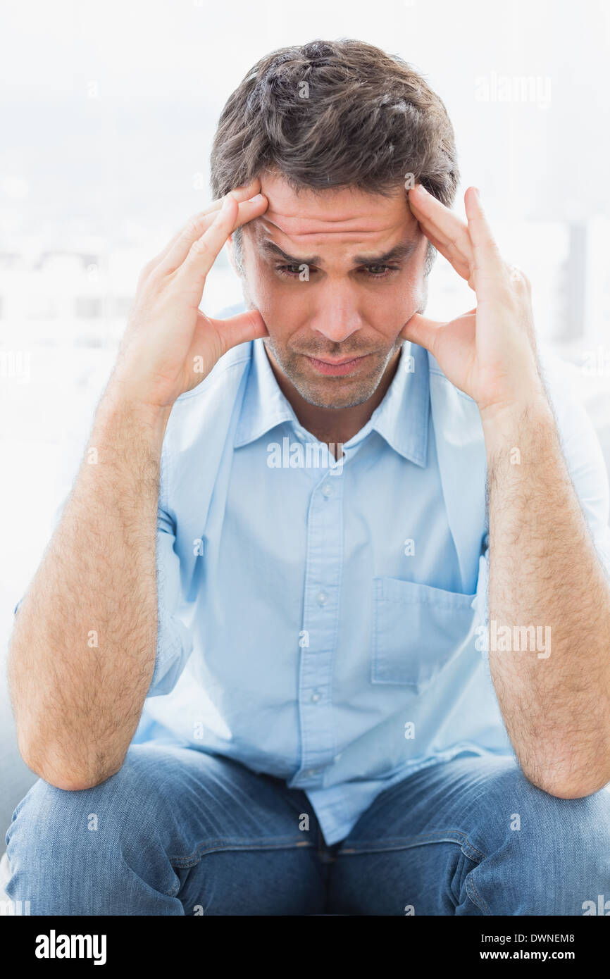 Wincing man with headache sitting on the couch Stock Photo