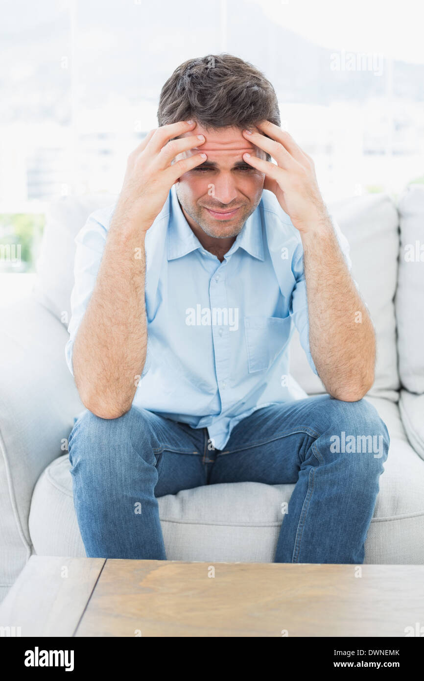 Handsome man sitting on the couch with headache looking at camera Stock Photo
