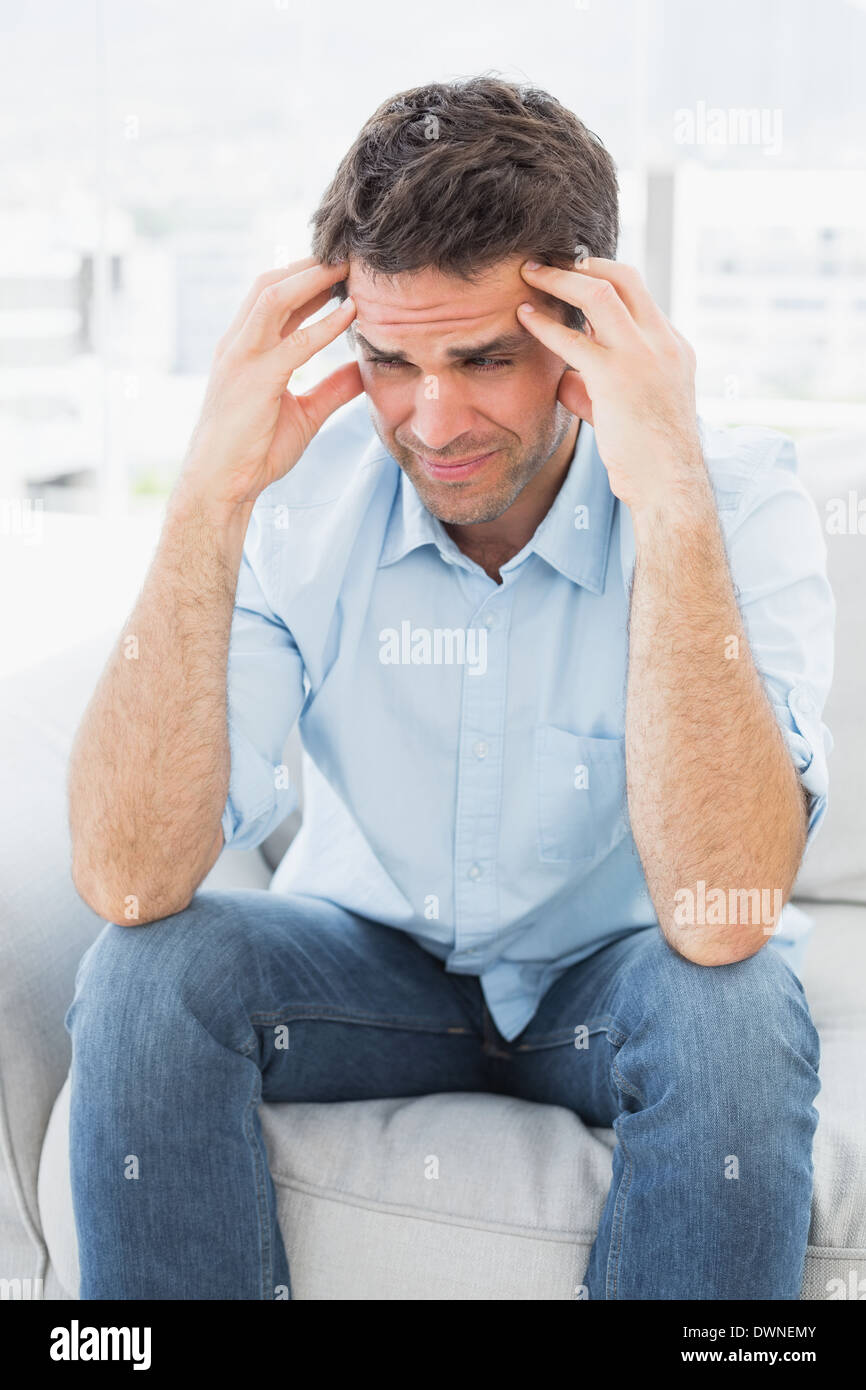 Grimacing man sitting on the couch with a headache Stock Photo