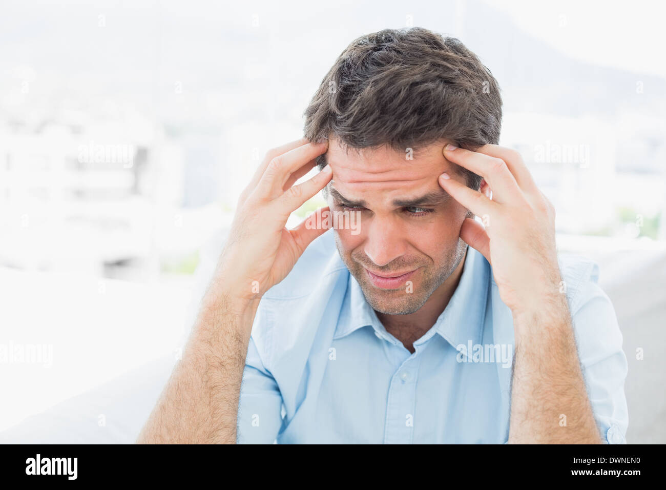 Frowning man sitting on the couch with a headache Stock Photo
