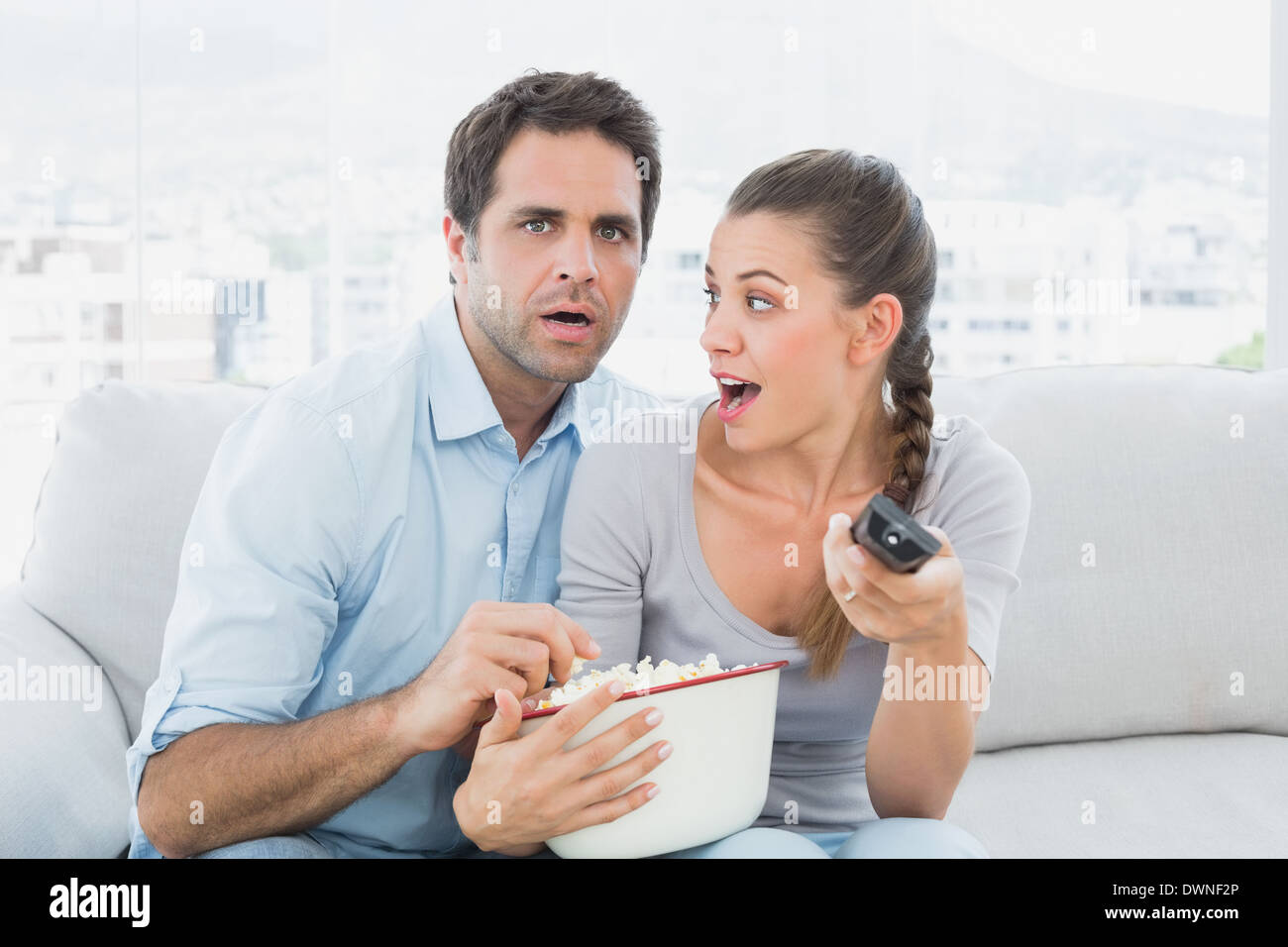 Couple watching scary movie on the couch with bowl of popcorn Stock