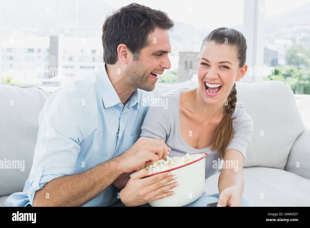 Couple watching funny movie on the sofa with bowl of popcorn Stock Photo