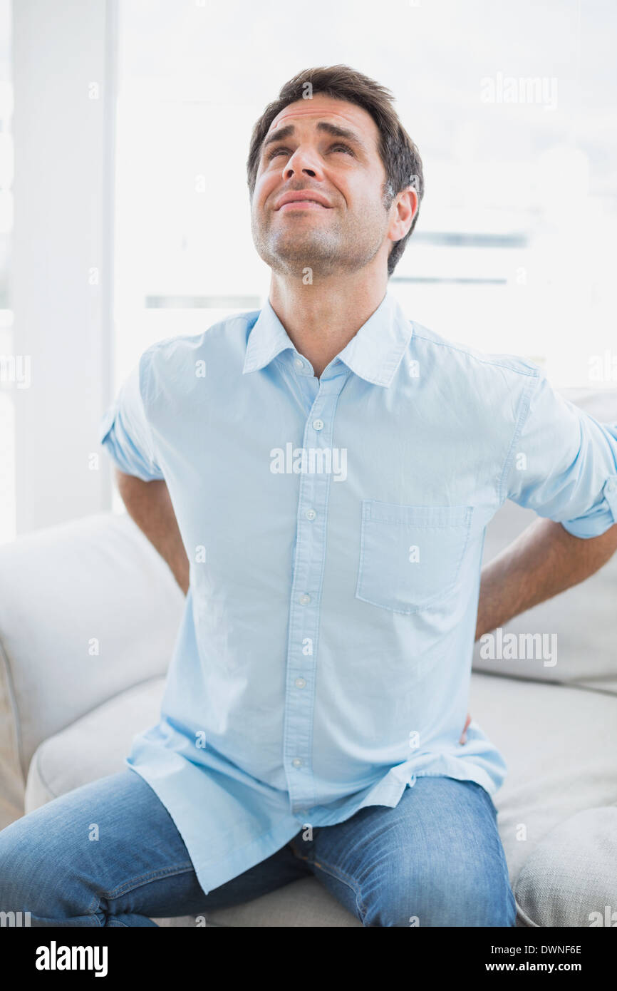 Handsome man sitting on sofa stretching painful back Stock Photo