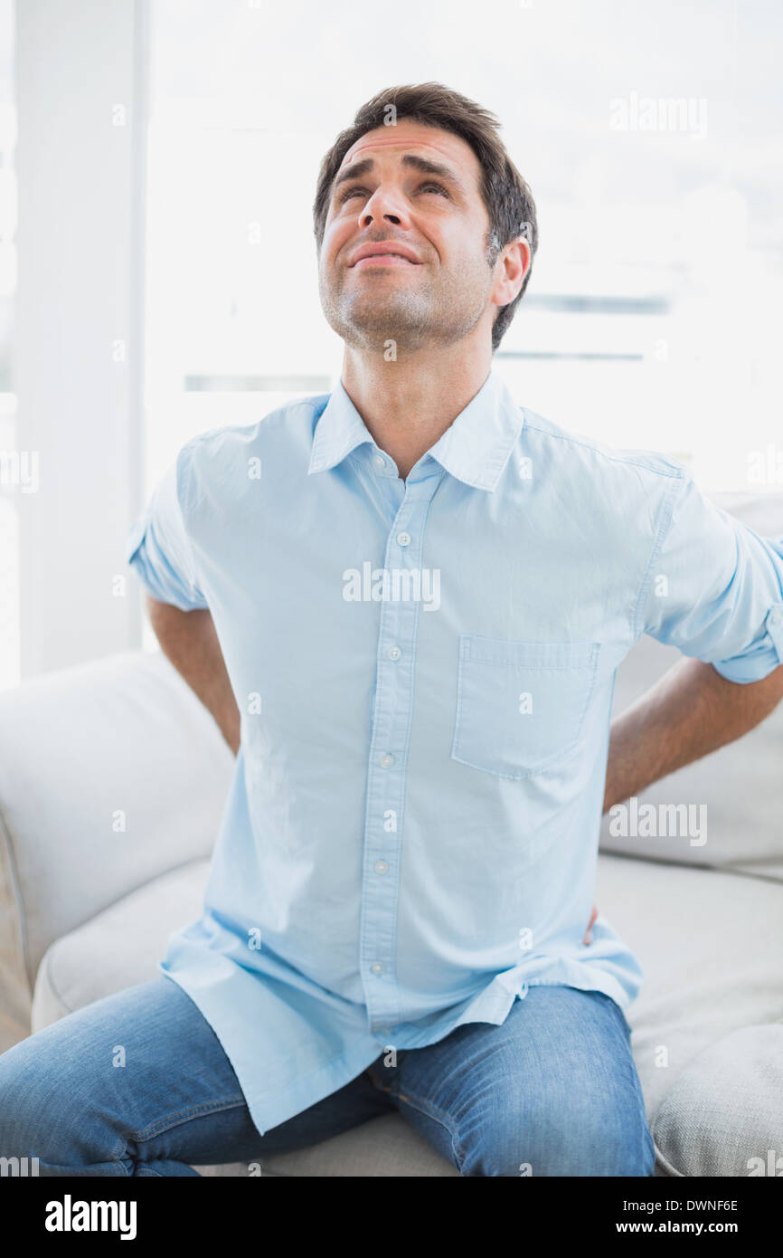 Handsome man sitting on sofa stretching painful back Stock Photo - Alamy
