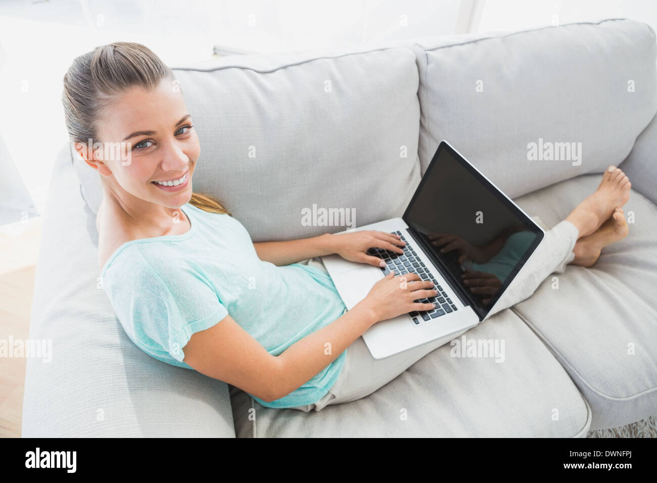 Happy woman sitting on couch using her laptop smiling up at camera ...