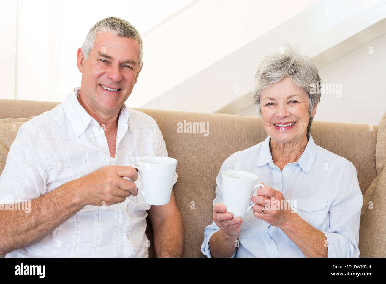 Senior couple sitting on couch drinking coffee smiling at camera Stock ...