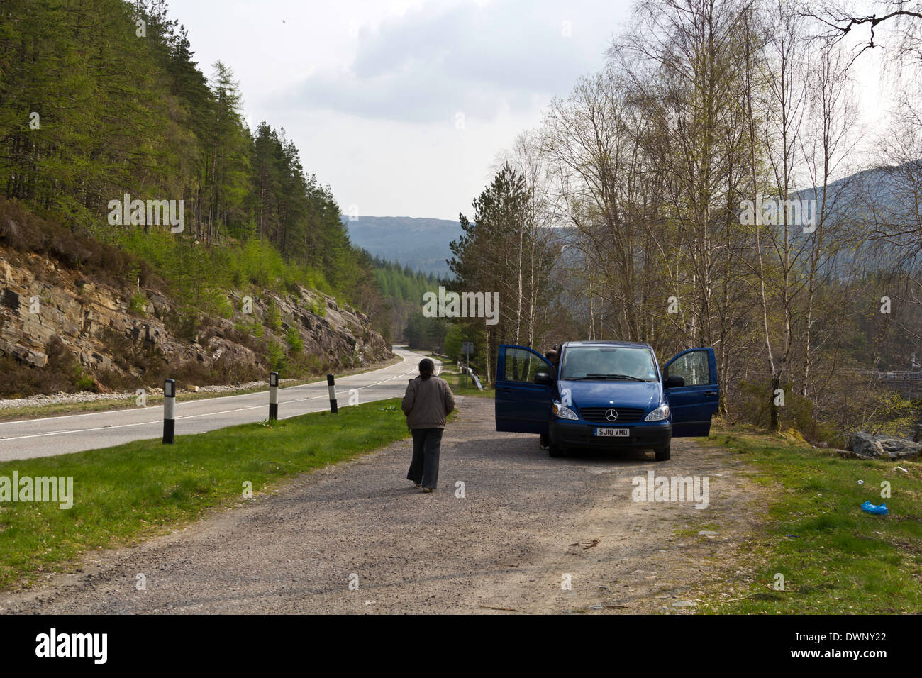 Parking next to a Loch in the Scottish Highlands, on a side parking road with greenery all around. Lady walking back to open van Stock Photo