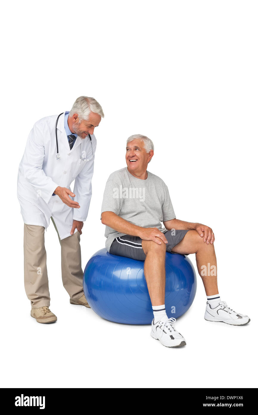 Male therapist looking at senior man sit on exercise ball Stock Photo