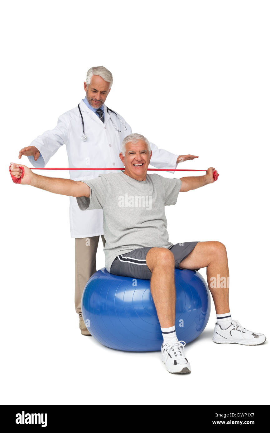 Mhysiotherapist looking at senior man sit on exercise ball with yoga belt Stock Photo