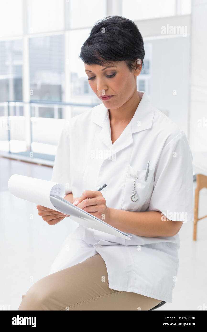 Concentrated female doctor writing on clipboard Stock Photo - Alamy