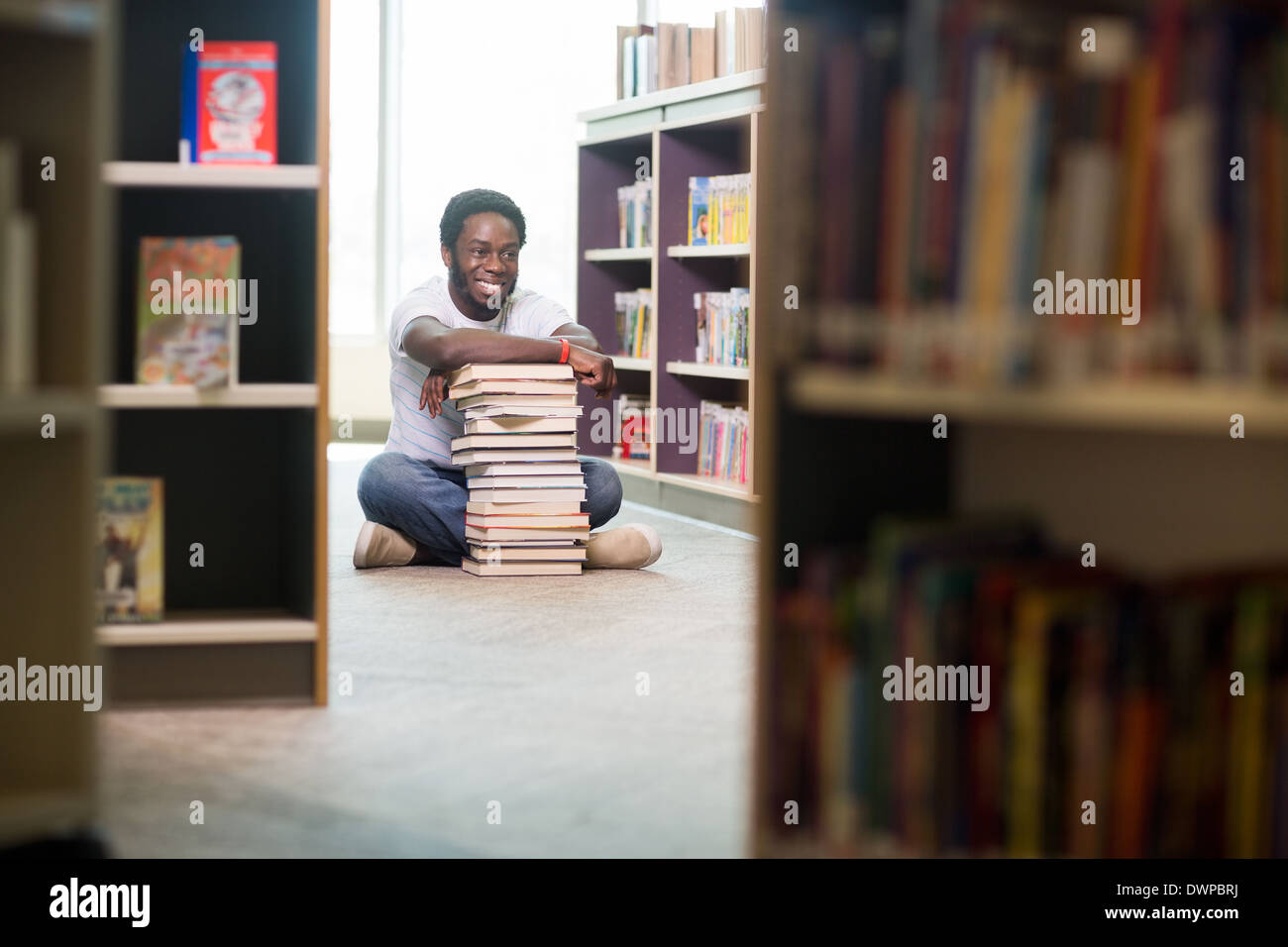 Happy Student With Stacked Books Sitting In Library Stock Photo - Alamy
