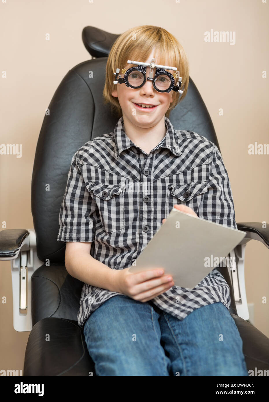 Boy With Trial Frame Holding Test Chart At Optician Stock Photo