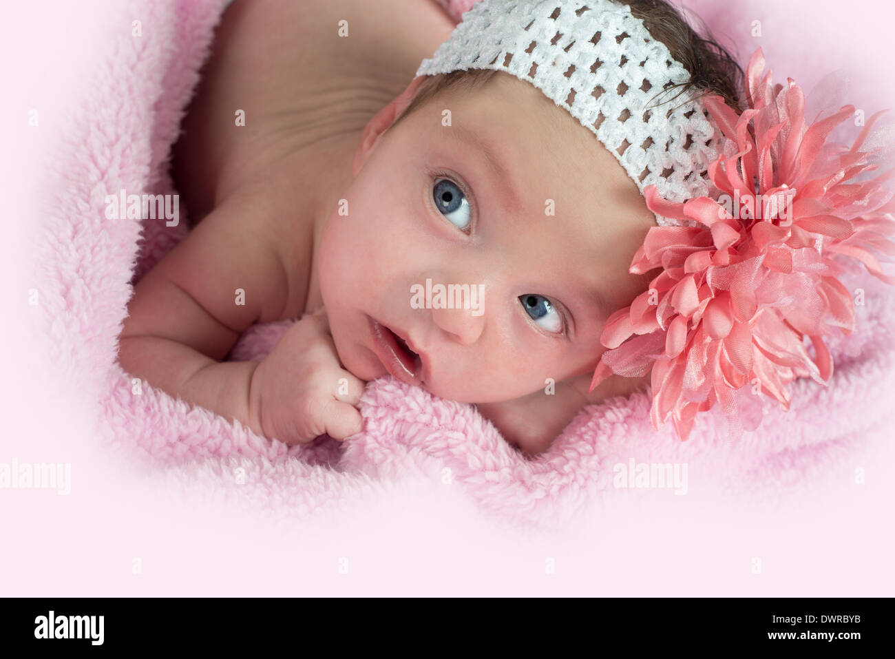 pretty blue eyed baby wearing a flower headband laying on a pink blanket looking up Stock Photo
