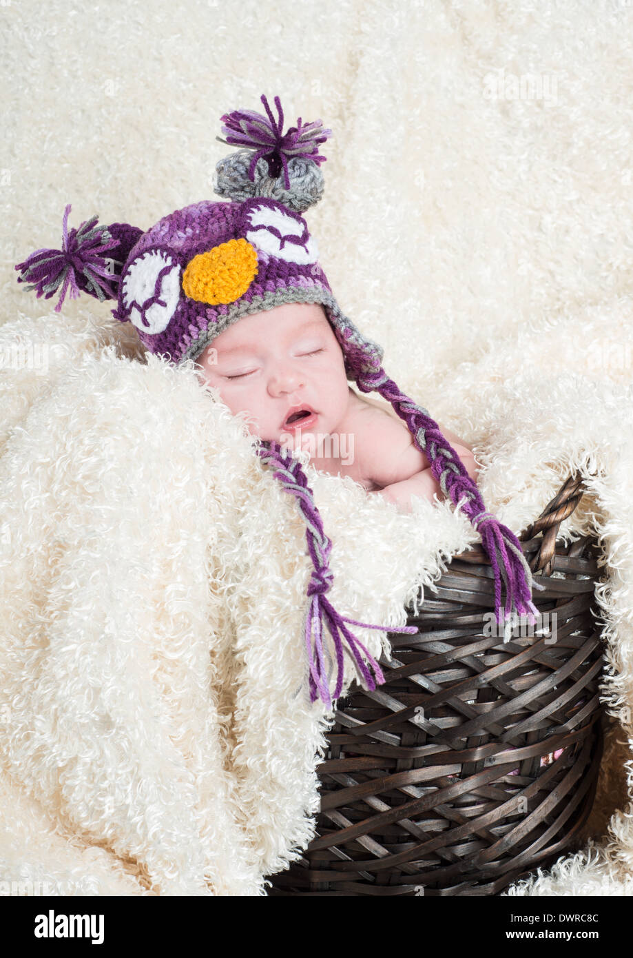 Sleeping baby in a basket with a soft blanket wearing a crocheted owl hat Stock Photo