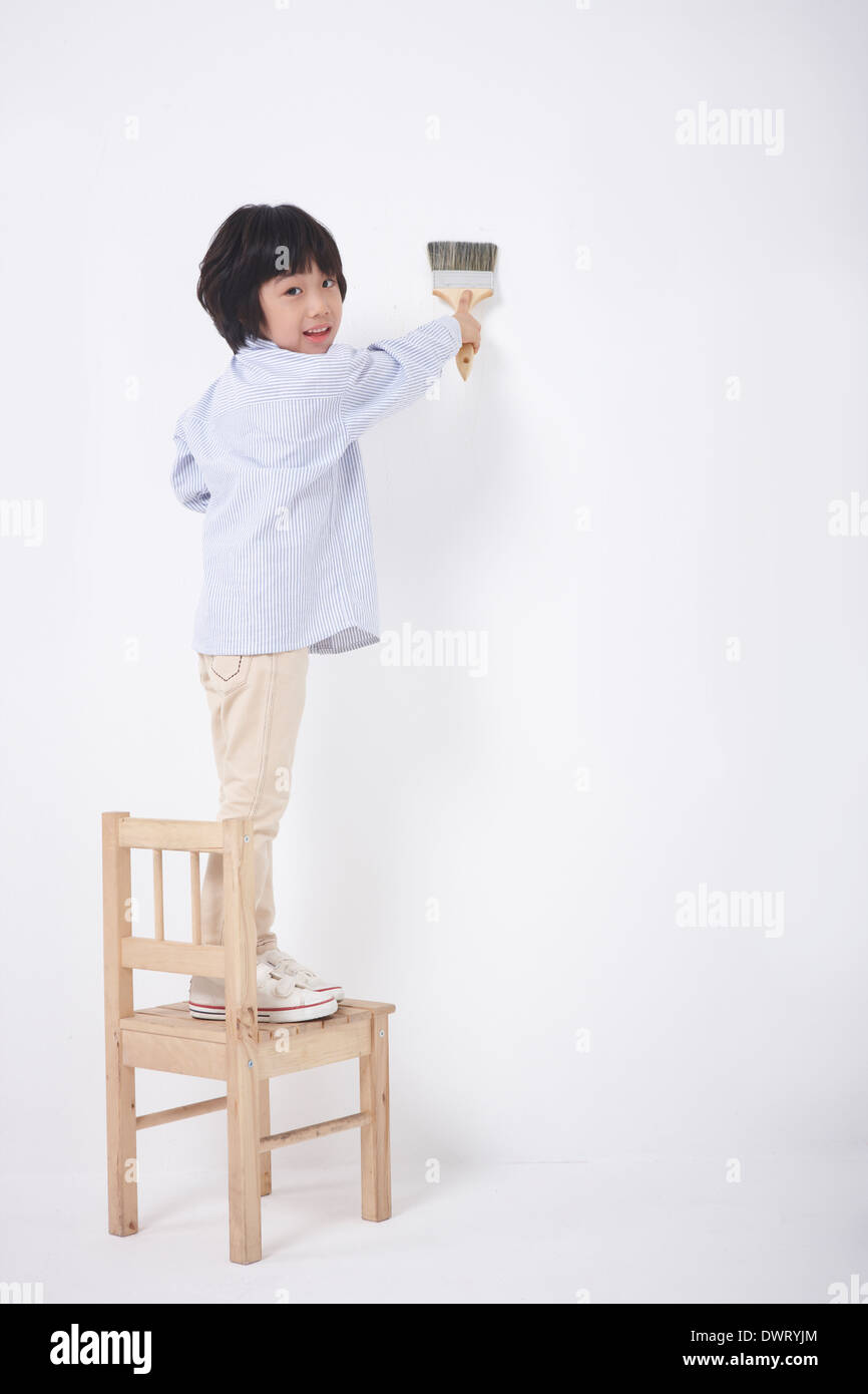 a kid painting wall standing on a chair Stock Photo