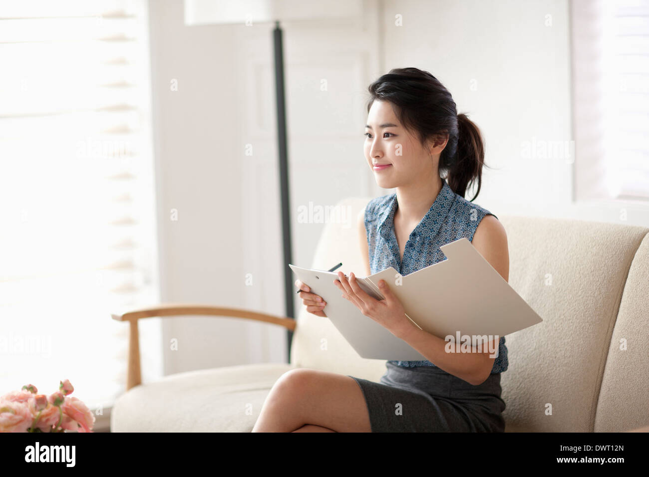 a woman sitting on a couch writing something on a folder Stock Photo ...