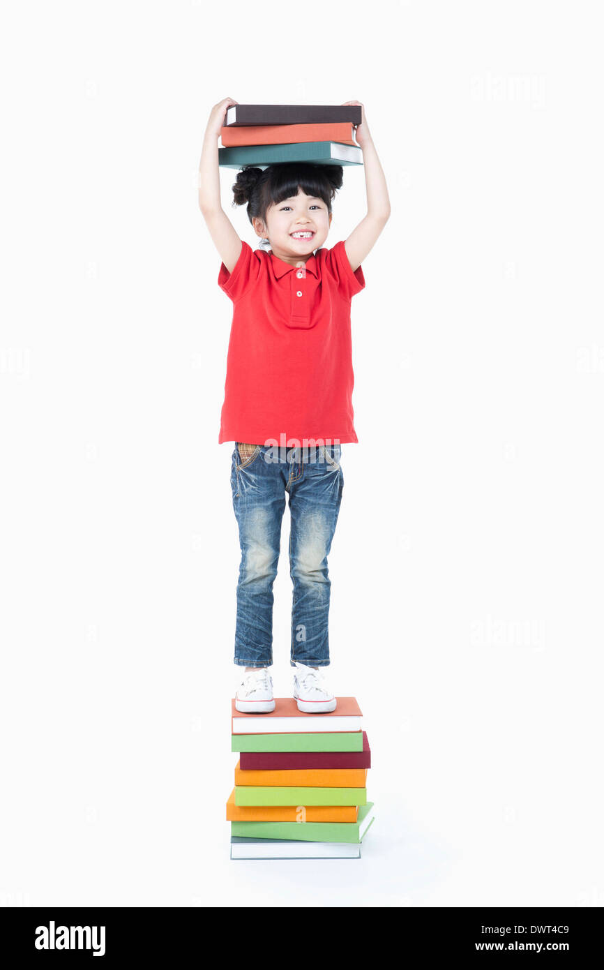 a kid standing on a pile of books while holding books Stock Photo