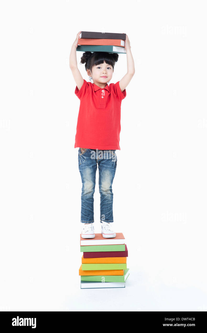 a kid standing on a pile of books while holding books Stock Photo