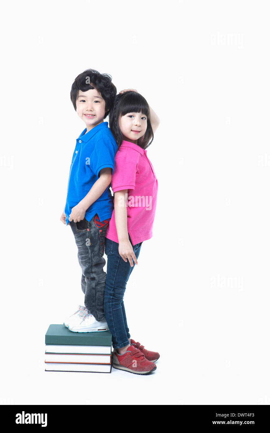 a boy standing on pile of books measuring height with a girl Stock Photo