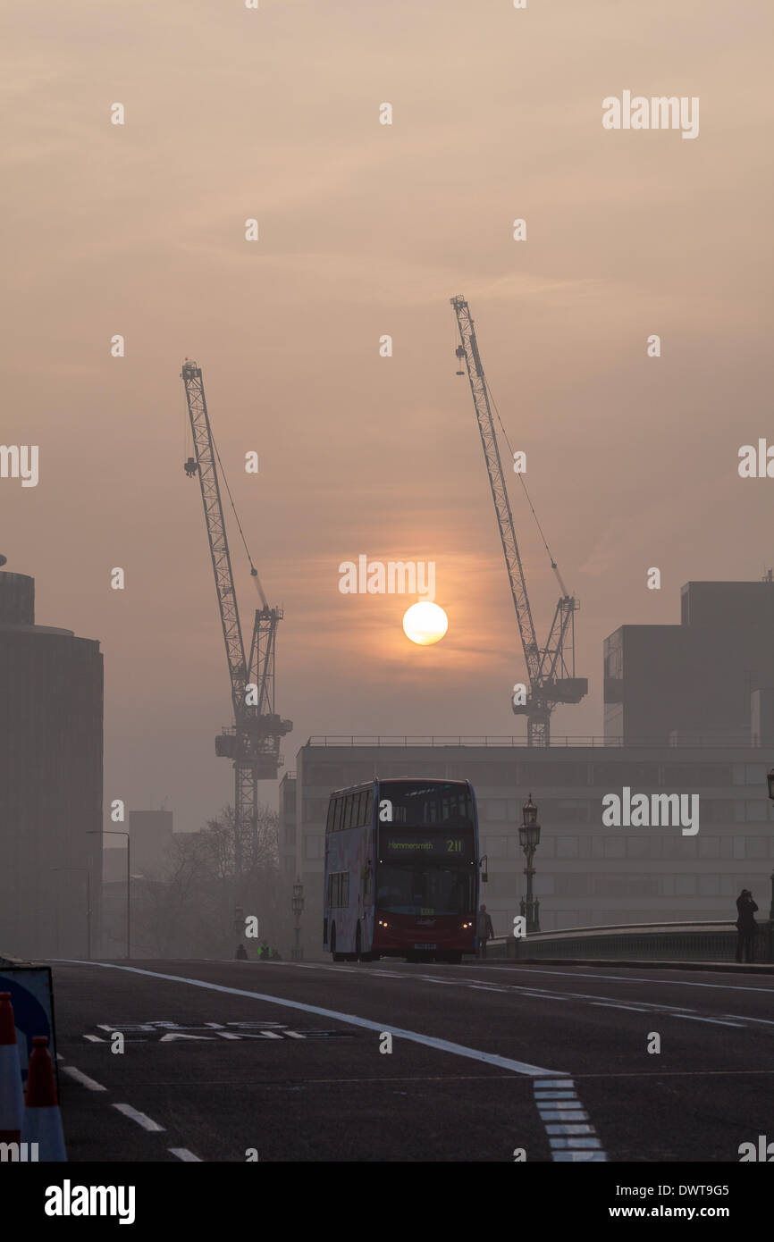 LONDON, UK, 13th Mar, 2014. London starts the day swathed in a blanket of fog. The sun rises behind cranes near St Thomas' Hospital, Westminster as a London bus crosses Westminster Bridge Credit:  Steve Bright/Alamy Live News Stock Photo