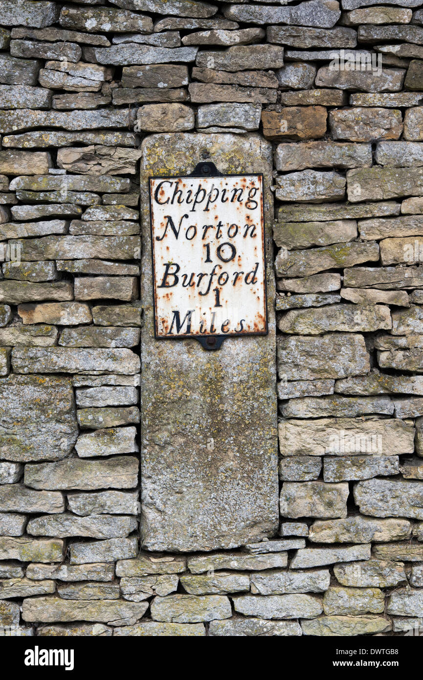 Old stone road sign embedded into a cotswold stone wall. Cotswolds, England Stock Photo