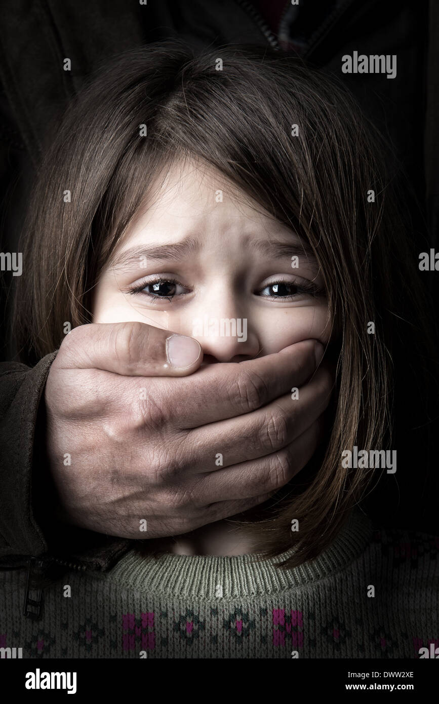 Scared young girl with an adult man's hand covering her mouth Stock Photo