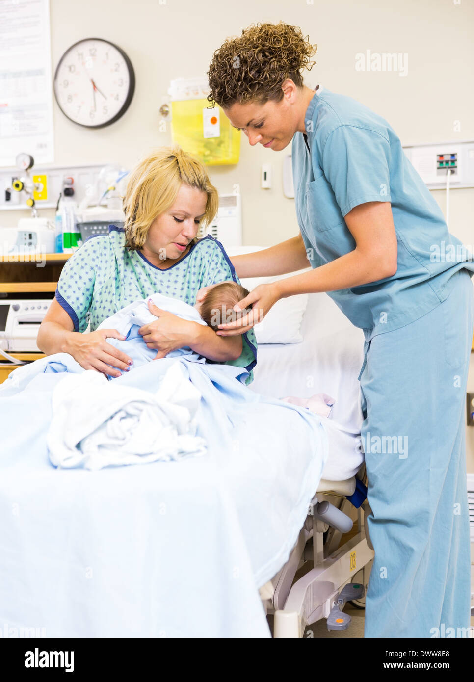 Nurse Helping Woman In Holding Newborn Baby At Hospital Stock Photo