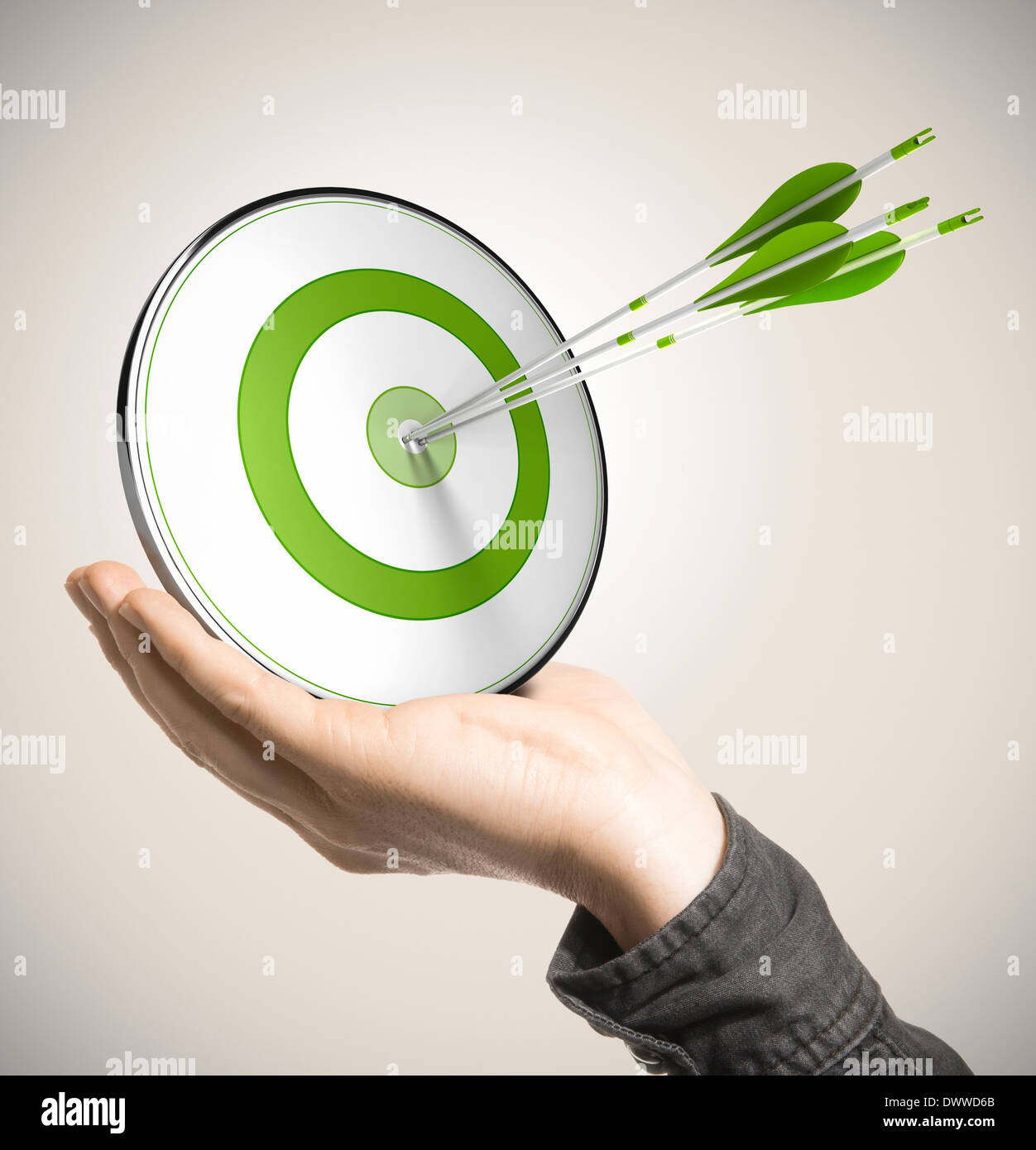 Hand holding a green target with three arrows hitting the center over beige background. Business performance concept. Stock Photo