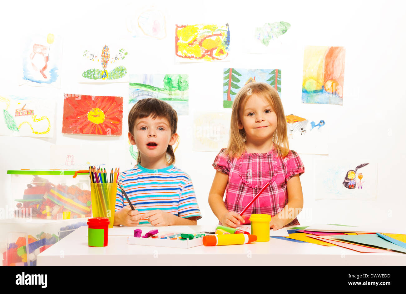 Two three years old kids sitting by the table with paints and brushes Stock Photo