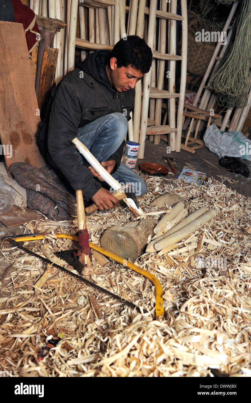 Woodworker in workshop using hand adze for shaping wood for chair part, Marrakech, Morocco, North Africa Stock Photo