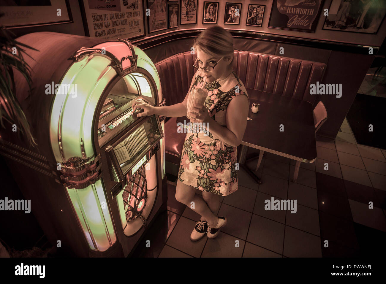 A 16-year-old Caucasian teenager wearing a 1950's, flowered dress stands next to a jukebox at an historic diner in Cortland, NY. Stock Photo
