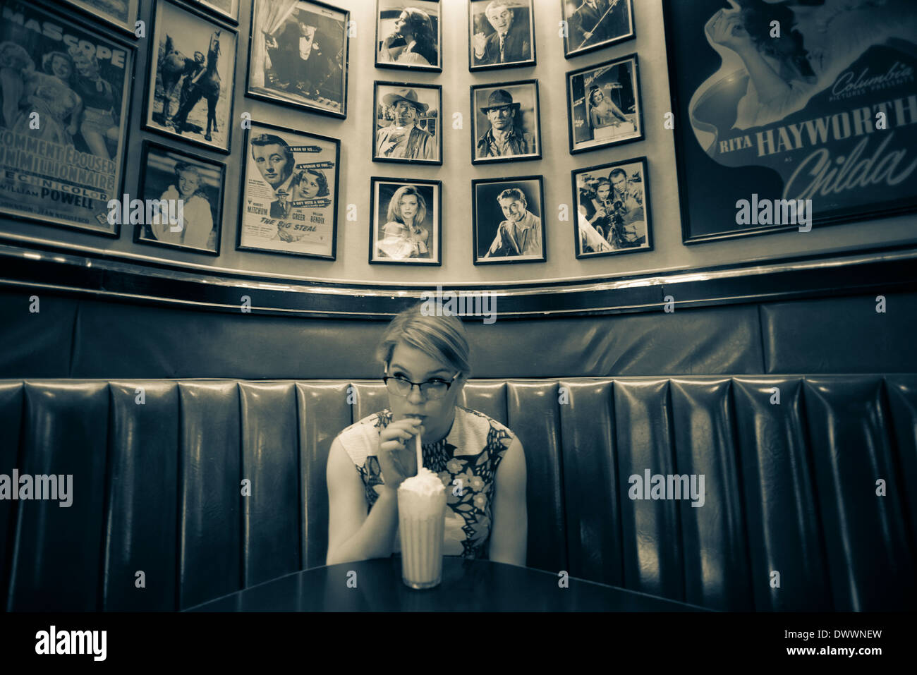 A 16-year-old Caucasian teenage girl wearing a 1950's, flowered dress sips a milkshake in an historic diner in Cortland, NY. Stock Photo