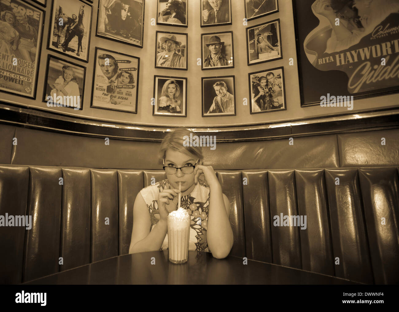 A 16-year-old Caucasian teenage girl wearing a 1950's, flowered dress sips a milkshake in an historic diner in Cortland, NY. Stock Photo