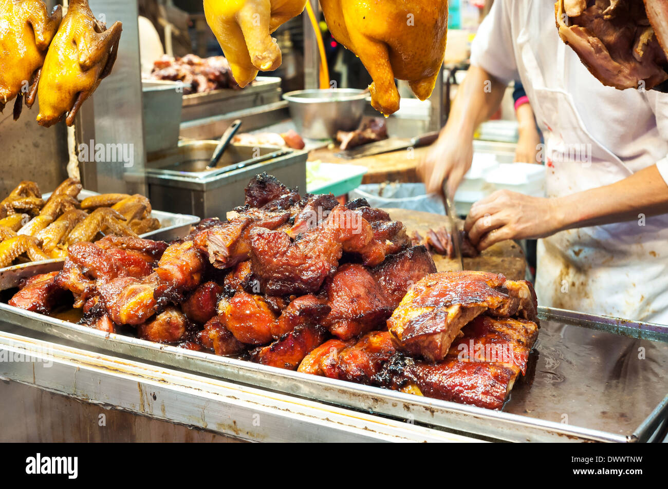 Butcher cutting barbequed pork, also known as cha siu, at a Hong Kong meat stall Stock Photo