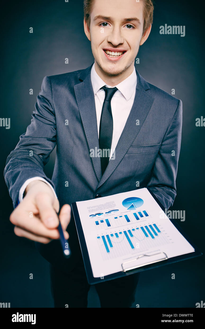 Portrait of a young businessman with document offering pen and looking ...