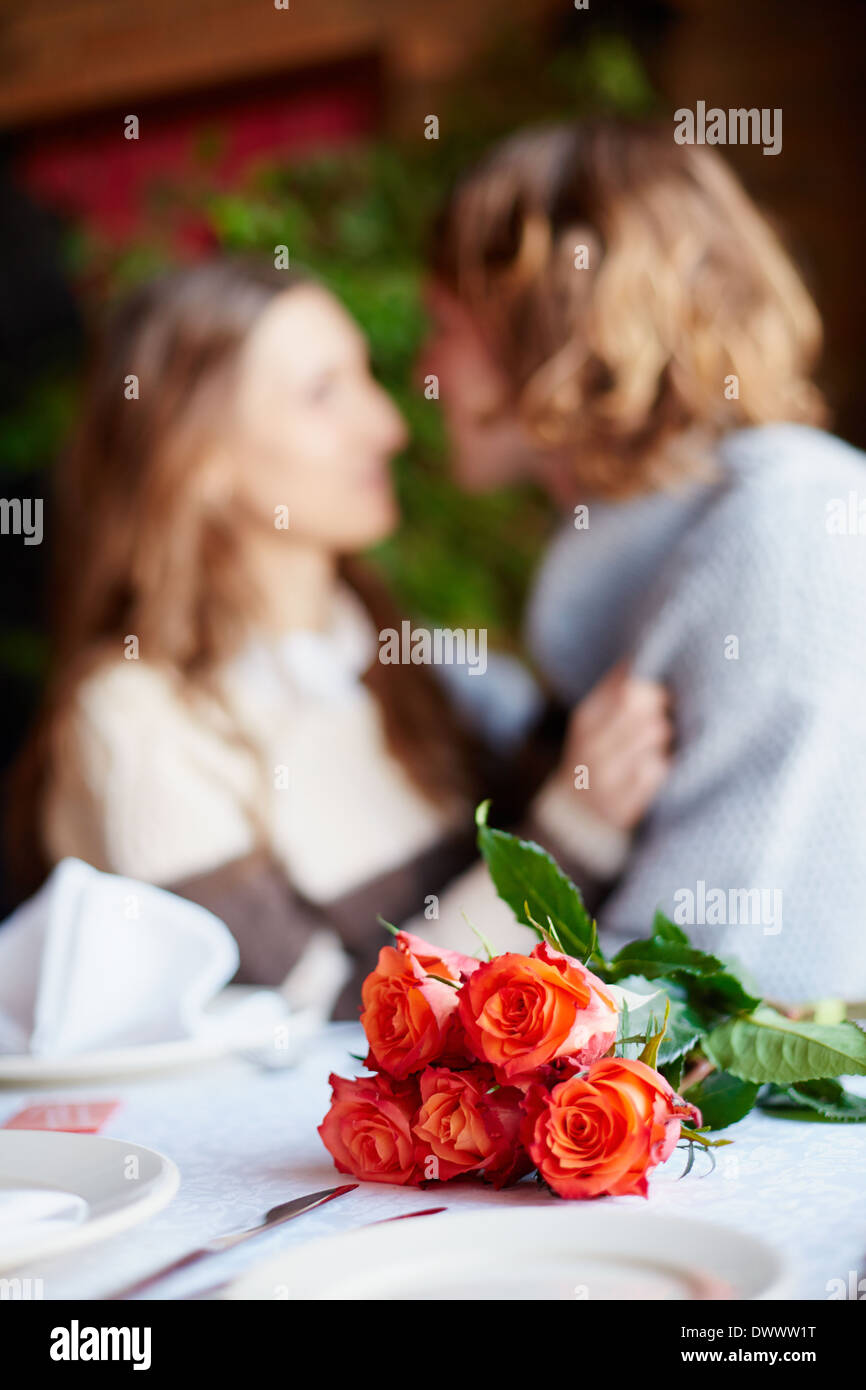 A bunch of red roses on served table and young lovers on background Stock Photo