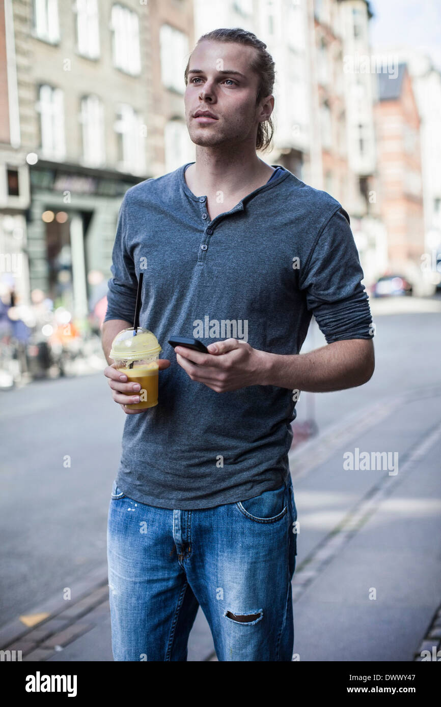 Young man with disposable cup and mobile phone standing on sidewalk Stock Photo