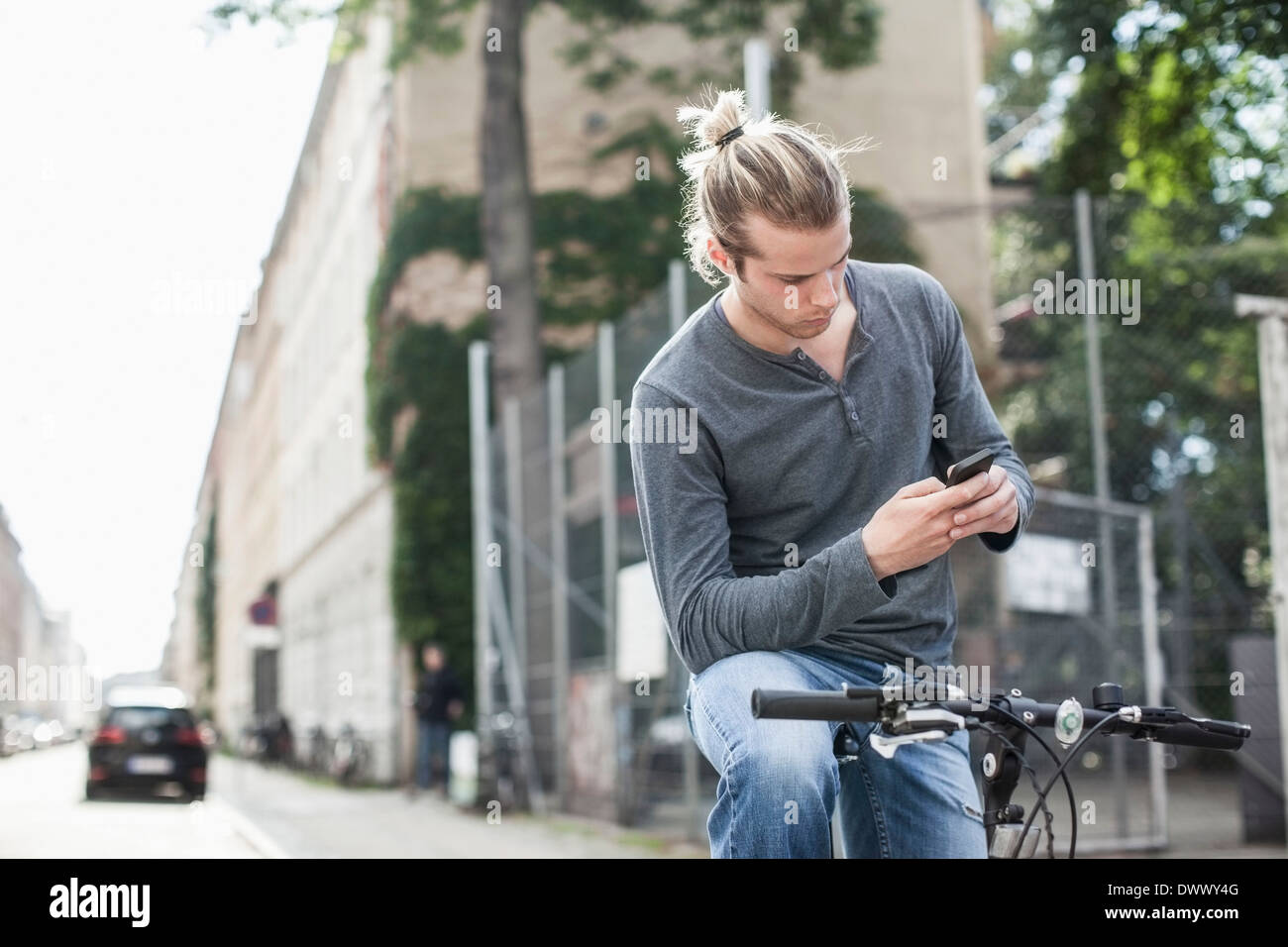 Young man text messaging through mobile phone while sitting on bicycle at street Stock Photo