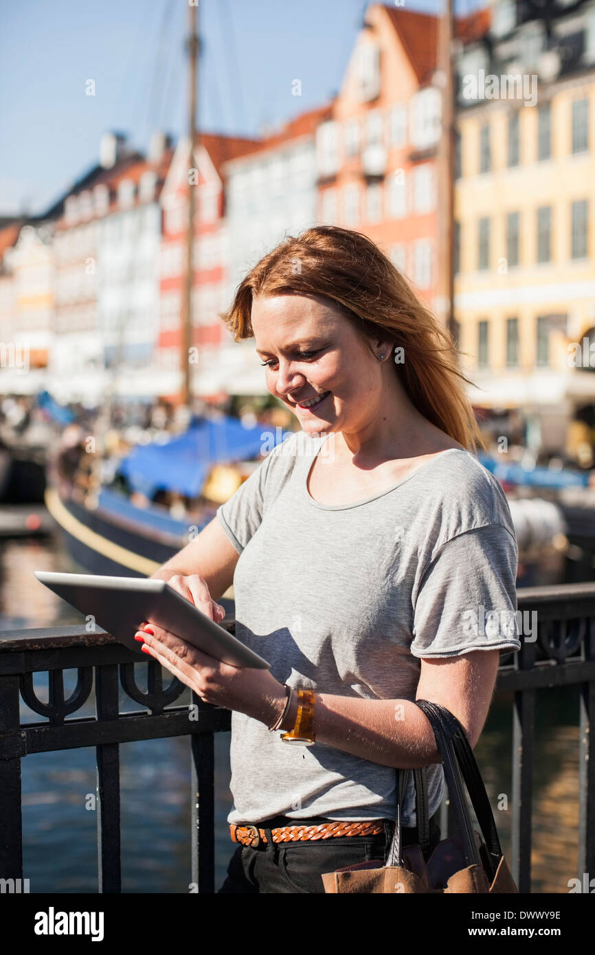 Smiling woman using digital tablet by railing at harbor Stock Photo