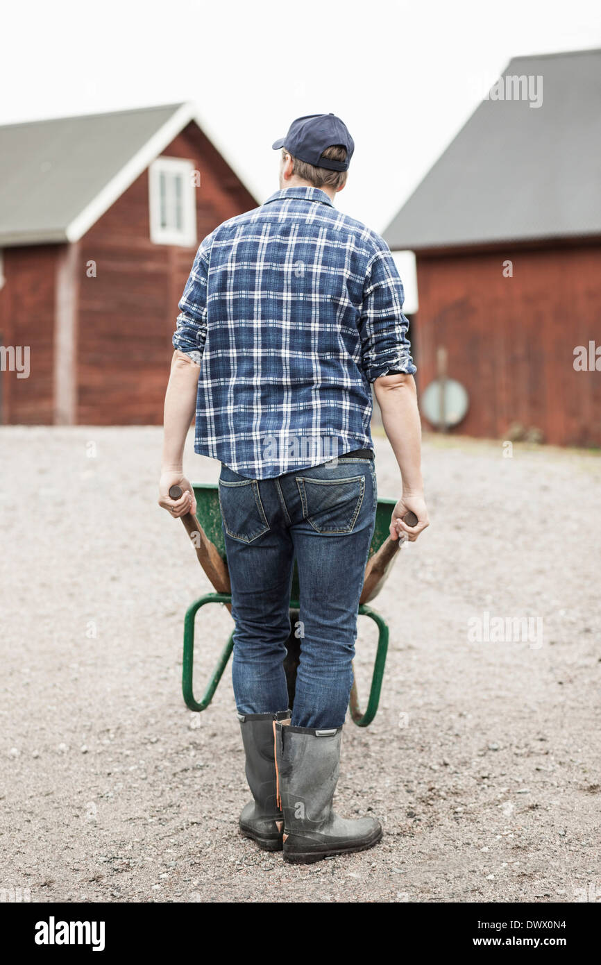 Rear view of farmer pushing wheelbarrow on rural road Stock Photo - Alamy