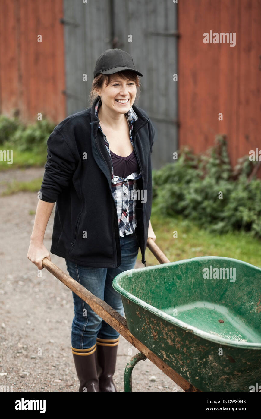 Happy female farmer with wheelbarrow against barn Stock Photo - Alamy