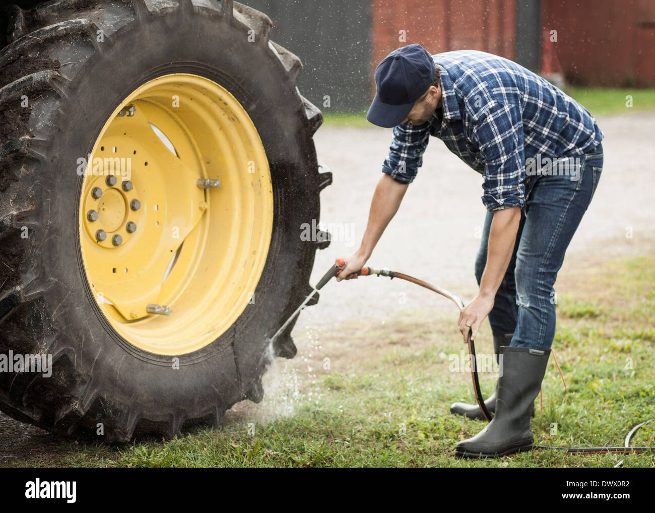 Full length of man washing tractor wheel with hose in farm Stock Photo