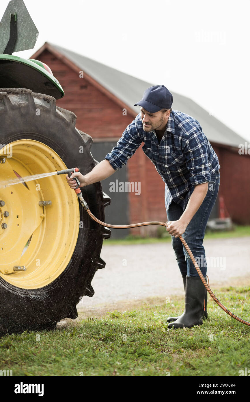 Full length mid adult man washing tractor wheel with hose in farm Stock Photo