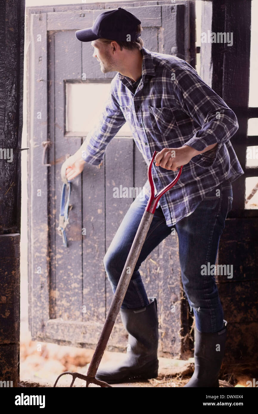Full length of farmer with pitchfork closing barn door Stock Photo