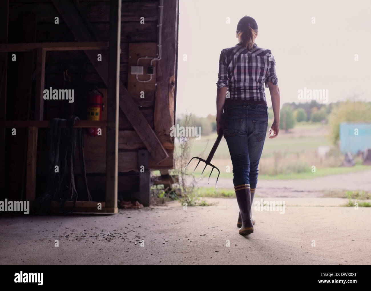 Rear view of female farmer with pitchfork walking in barn Stock Photo